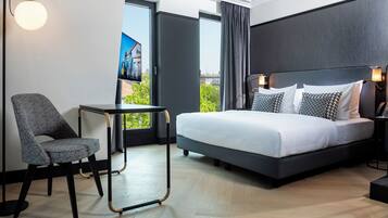 A modern hotel room with a large bed, a small table, a chair, and a TV.