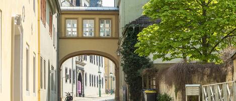 Una calle empedrada con un arco de piedra, edificios a ambos lados y un árbol en primer plano.