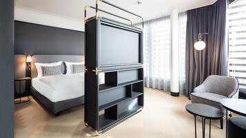 A modern hotel room with a bed, a TV stand, a chair, and a small table.