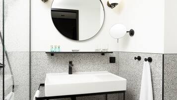 A modern bathroom with a white sink, a round mirror, and a black shelf.