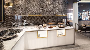 Une cuisine moderne avec un dosseret à motifs en chevrons, un plan de travail blanc agrémenté de touches dorées, ainsi que divers appareils de cuisine et ustensiles.