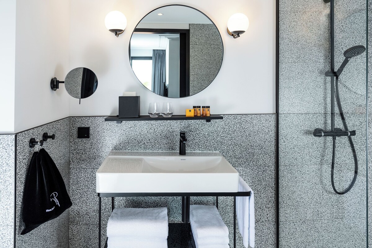 A modern bathroom with a round mirror, a white sink, and a shower.