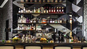 Una zona de bar con varias estanterías llenas de botellas de licor, una máquina de café y una exhibición de frutas.