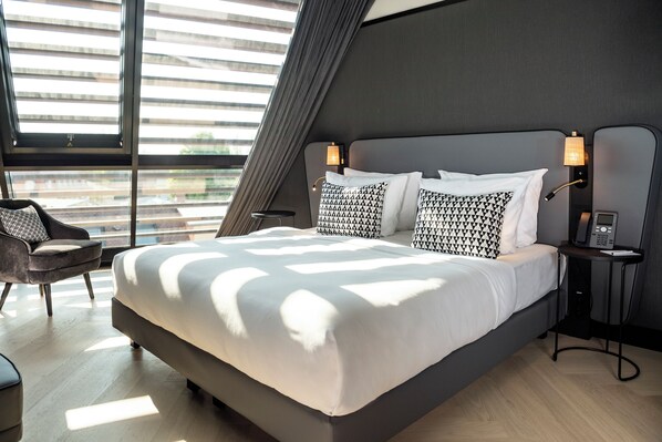 A modern hotel room with a large bed, two bedside tables, a chair, and large windows with blinds. - Hotel Schillerhof Weimar (Weimar)