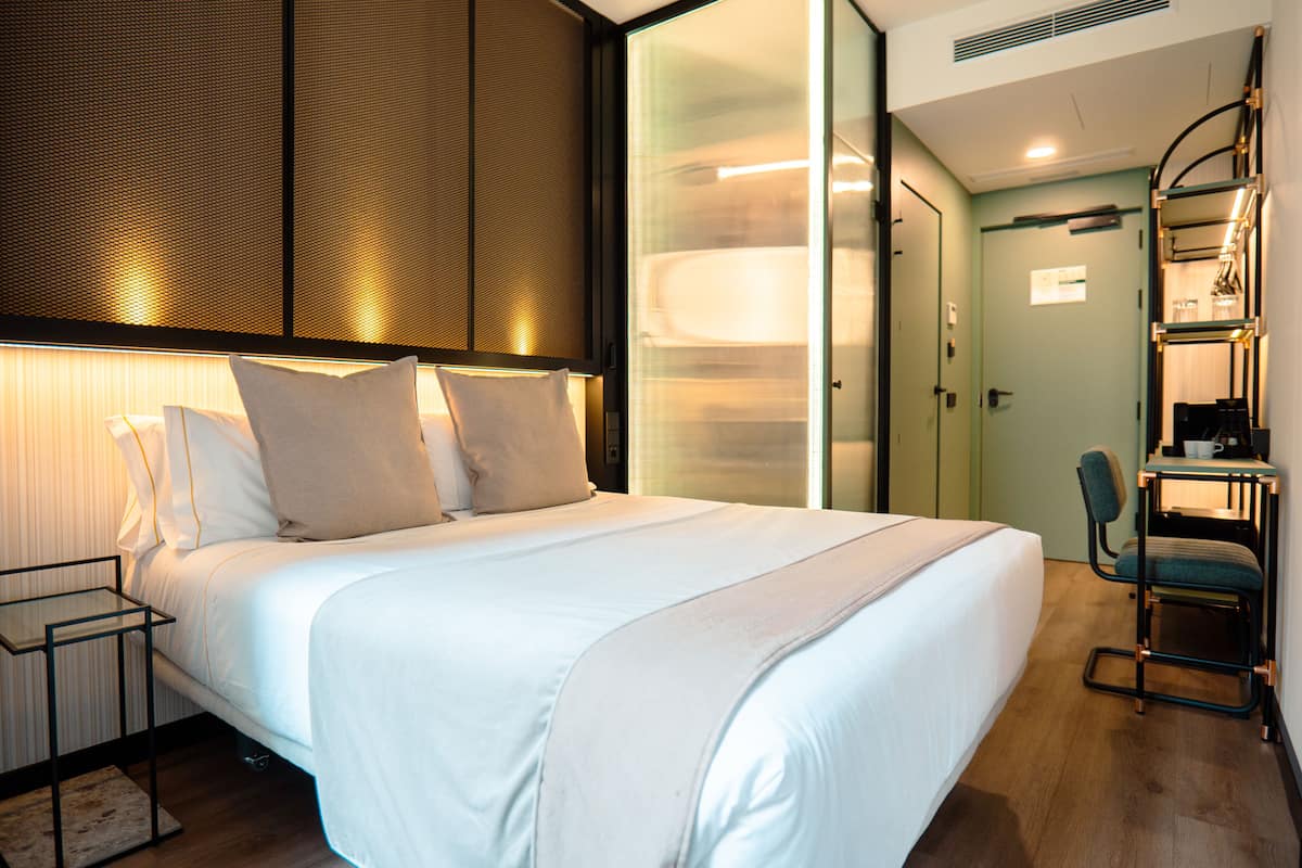 Ein modernes Hotelzimmer mit einem großen Bett, einem Schreibtisch mit Stuhl und einer Glaswand.