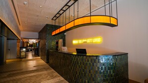 A reception area with a curved reception desk, a laptop on the desk, and a neon sign that reads "Where the City Lives". - Akeah Hotel Gran Via (Madrid)