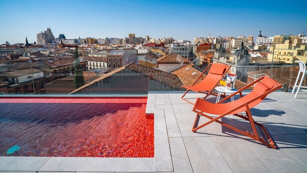 A rooftop terrace with a pool, orange lounge chairs, and a city view. - Akeah Hotel Gran Via (Madrid)