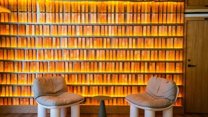 A seating area with two chairs and a small table, a wooden wall with a warm light, and a wooden door in the background. - Akeah Hotel Gran Via (Madrid)