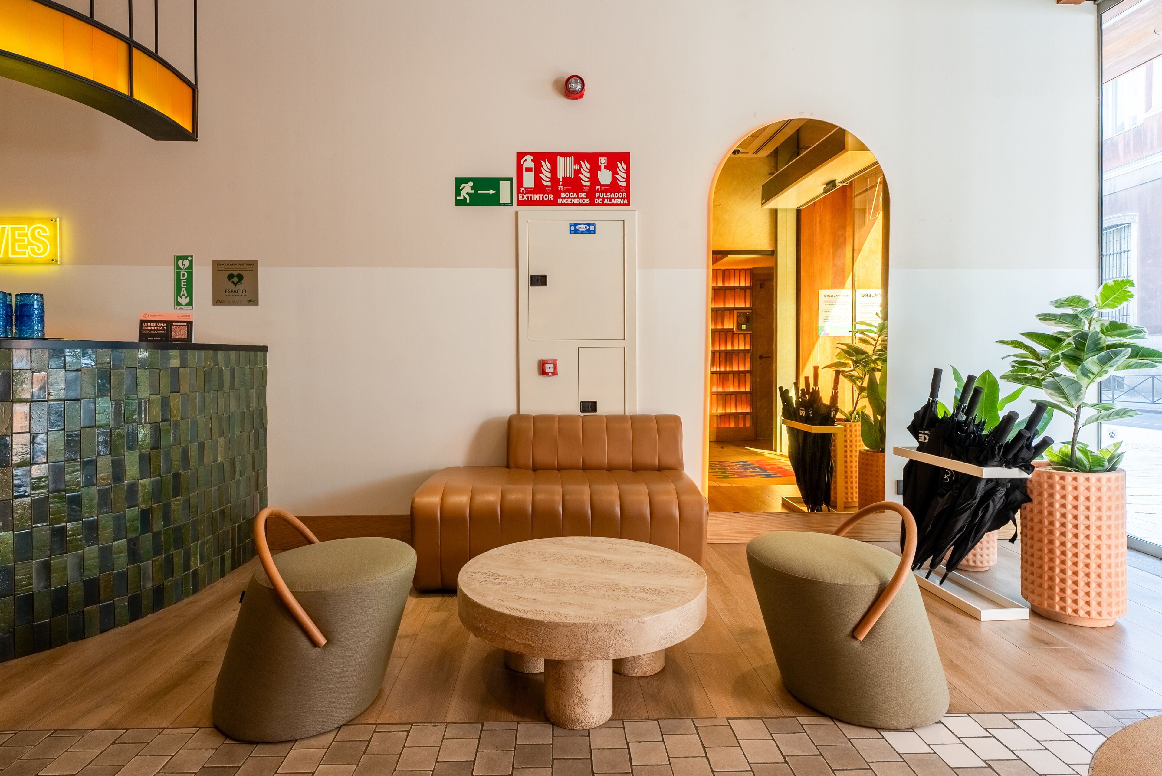 A modern lobby with a round table, two armchairs, a brown sofa, a reception desk, and an exit sign.