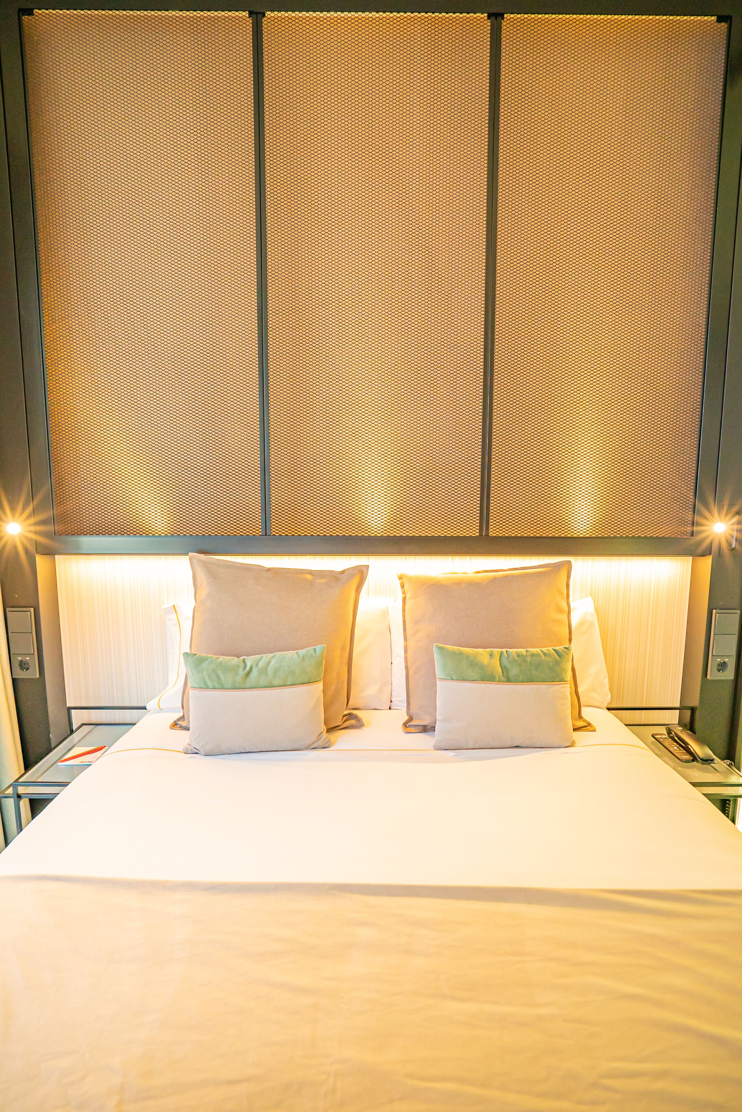 Una habitación de hotel con una cama grande, dos almohadas y un cabecero con panel texturizado.