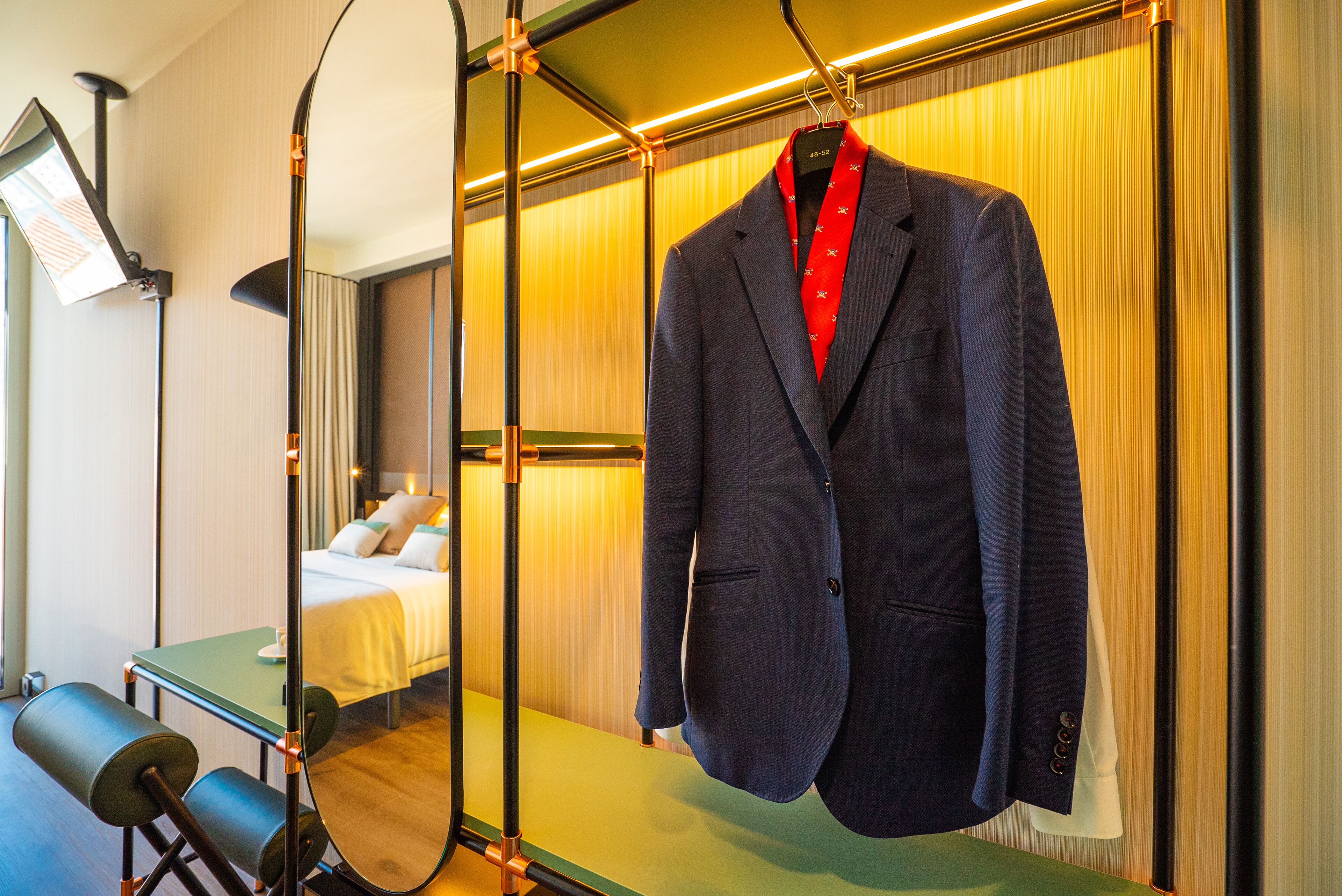 Une chambre d’hôtel avec un lit bien fait, un bureau avec une chaise et un costume suspendu à un cintre.