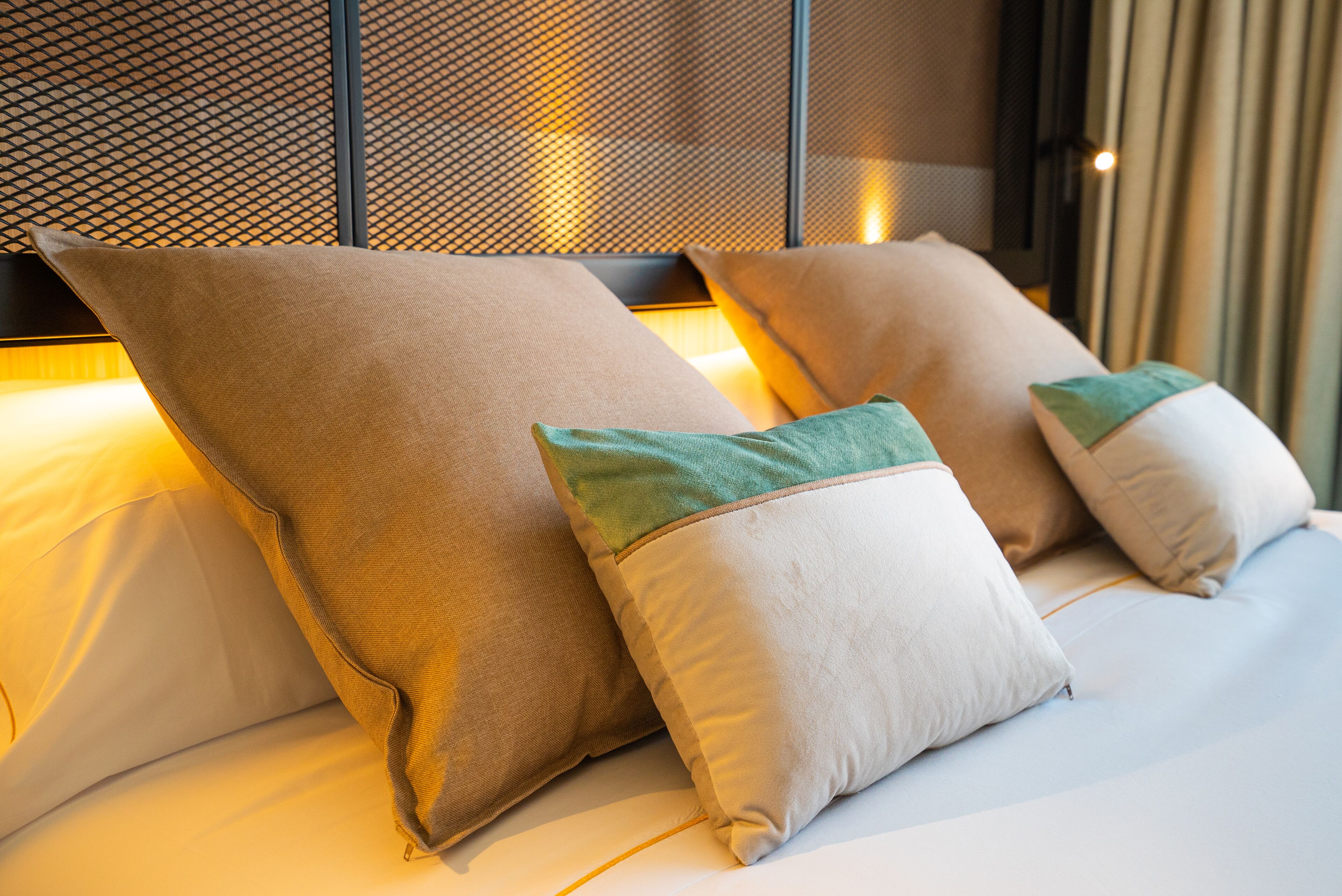 A neatly made bed with two large pillows and two smaller pillows with green accents.