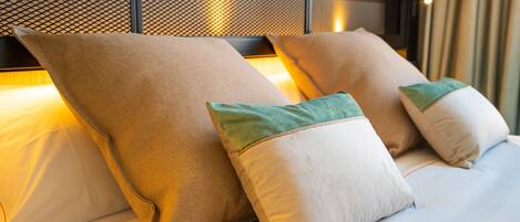 A neatly made bed with two large pillows and two smaller pillows with green accents.
