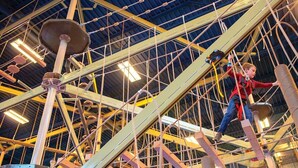 Eine Person überquert eine Seilbrücke in einer Industrieanlage, mit Metallträgern und Sicherheitseinrichtungen.