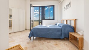 A bedroom with a bed, a wooden nightstand, a window with a view, and a wardrobe.
