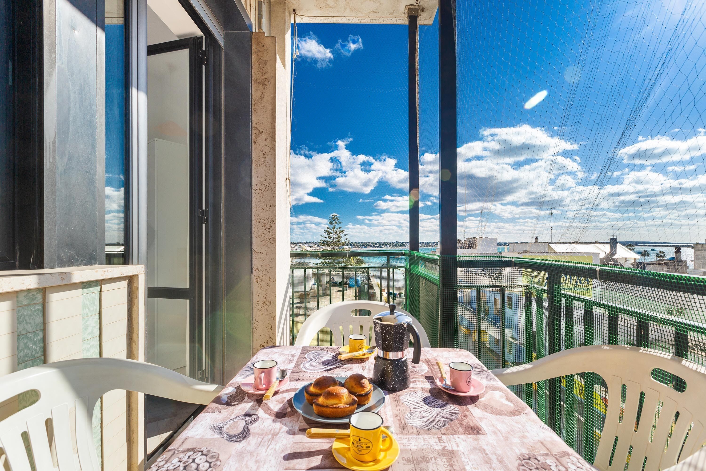 Un tavolo sul balcone con articoli per la colazione, vista sul mare e cielo sereno.
