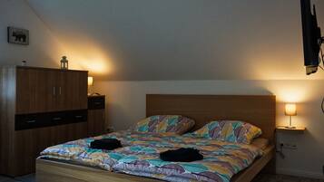 A bedroom with a wooden bed, two bedside lamps, a wardrobe, and a wall-mounted TV.