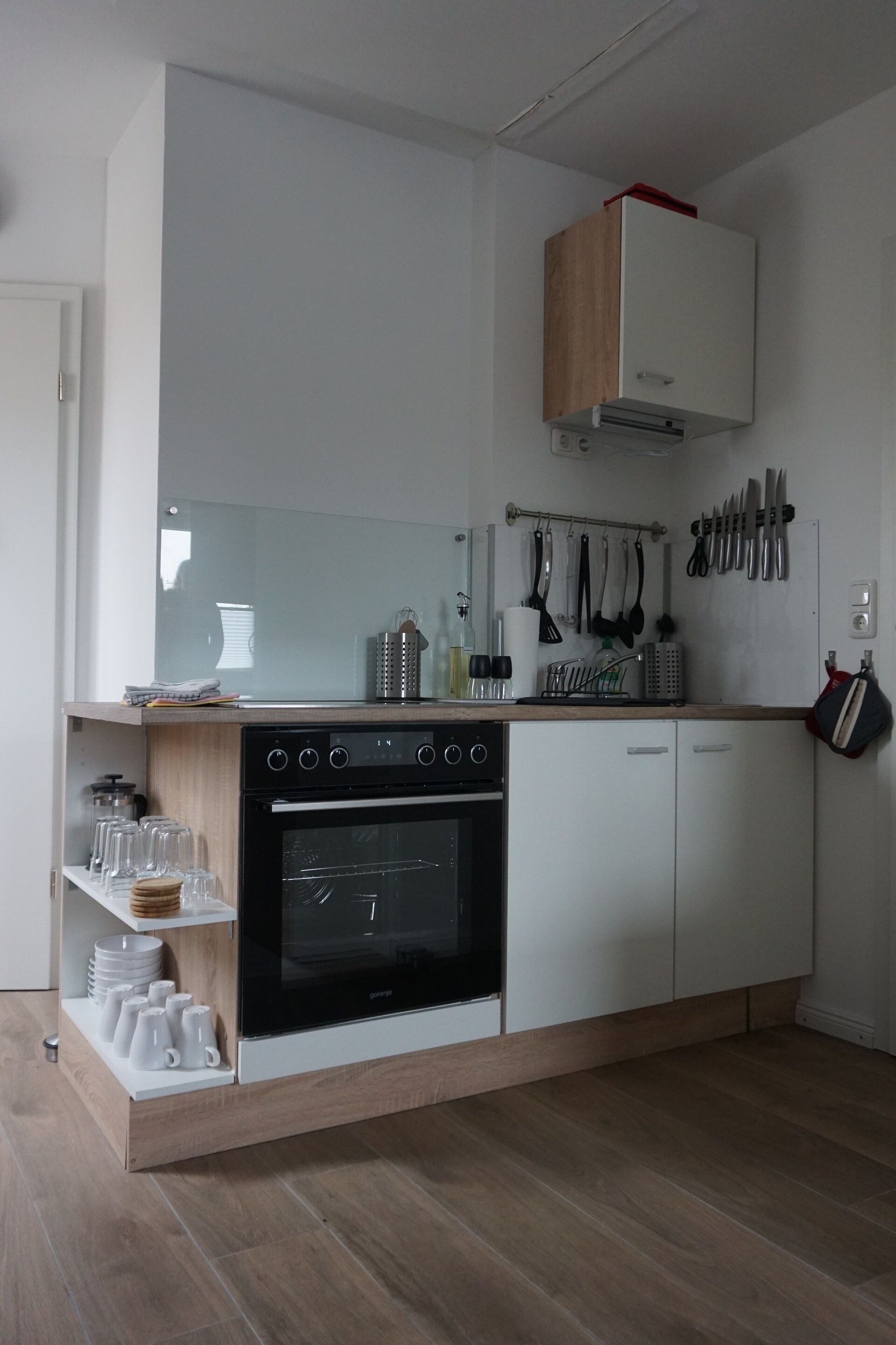 Une cuisine moderne dotée d’un four encastré, de meubles blancs et d’un plan de travail en bois.
