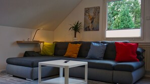 A modern living room with a grey sectional sofa, a white coffee table, and a window with a view of trees. - 2 cozy apartments, near Heide Park - approx. 10 min walk, FeWo Friedrichseck (Soltau)