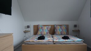 A bedroom with a wooden bed, two pillows with a leaf pattern, a bedside table with a lamp, and a TV mounted on the wall. - 2 cozy apartments, near Heide Park - approx. 10 min walk, FeWo Friedrichseck (Soltau)