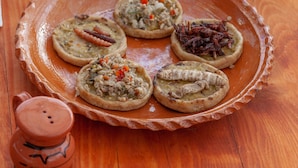 A wooden table with a clay plate holding several food items, a clay pot, a bowl of sauce, and a small clay pot with a lid. - Glamping Octli - Santuario de las Luciernagas X NANTLI LIVING (Nanacamilpa)