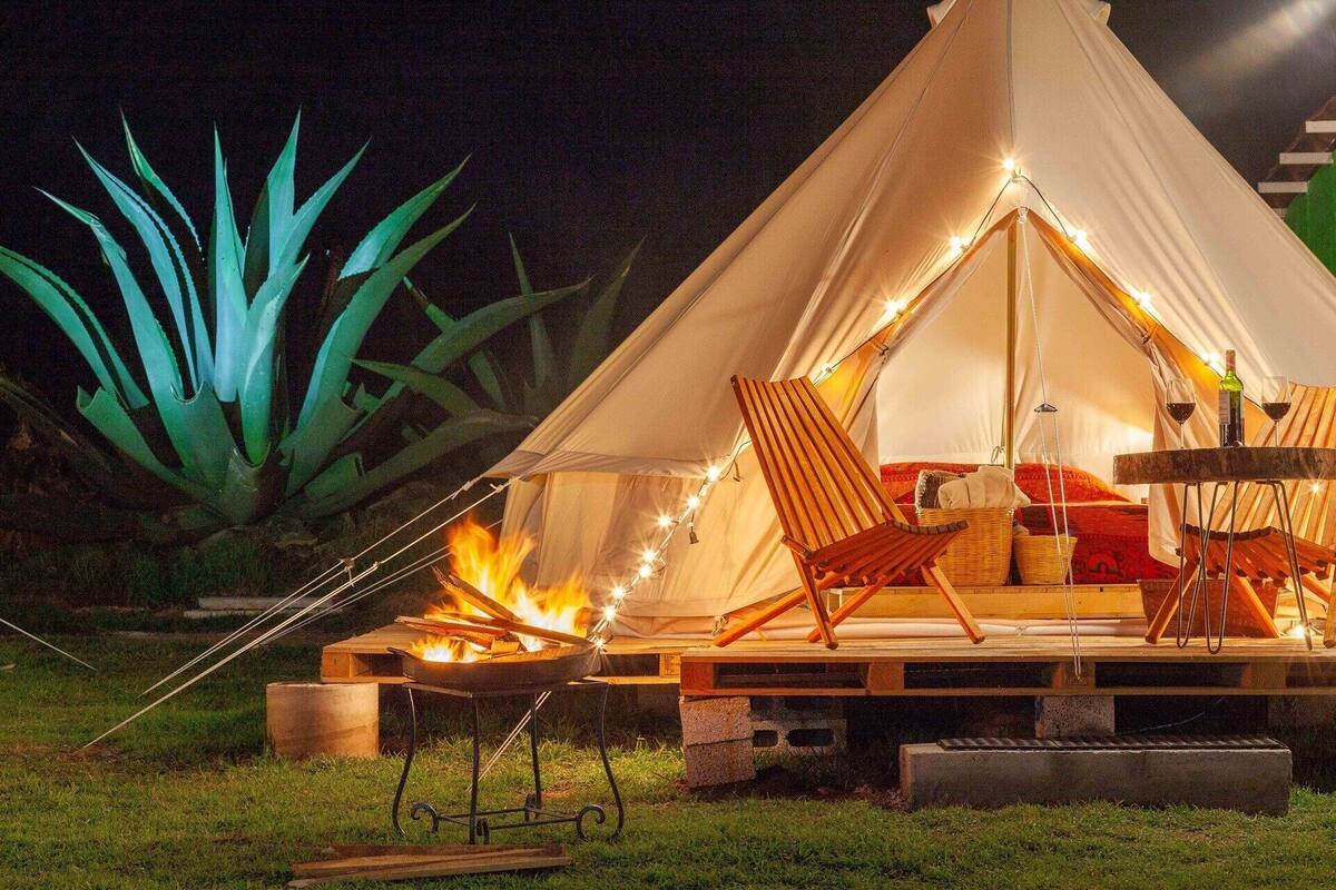 A tent with a fire, two chairs, a table, and a bottle of wine.