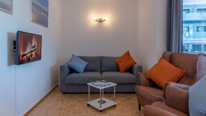 A living room with a grey sofa, a brown armchair, a small white table, and a wall-mounted light fixture. - Apartment Six T Nine, balcony, near ski lift (Zell am See)