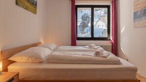 A double bed with white linens and two pillows, a bedside table with a lamp, a window with pink curtains, and a painting on the wall. - Apartment Six T Nine, balcony, near ski lift (Zell am See)