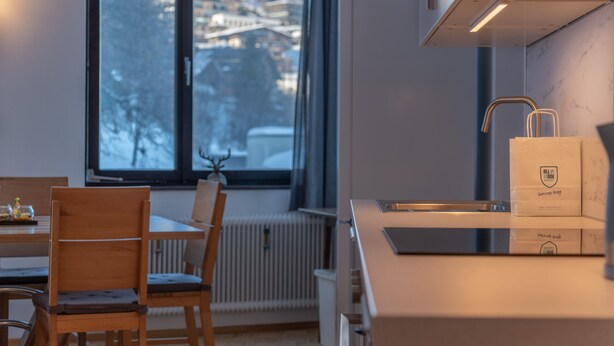A modern kitchen with a window view, wooden chairs, a countertop, and a bag of All in One serving bags. - Apartment Six T Nine, balcony, near ski lift (Zell am See)