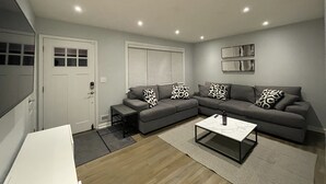 A modern living room with a sectional sofa, a coffee table, and a door with a window. - Newly renovated 3BR/2BA home - 10 mins from EWR (Elizabeth)