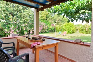 Um pátio externo com mesa e cadeiras de madeira, uma taça de vinho e uma garrafa de vinho.