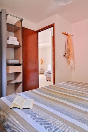 Quarto com cama, guarda-roupa de madeira e porta para outro cômodo.