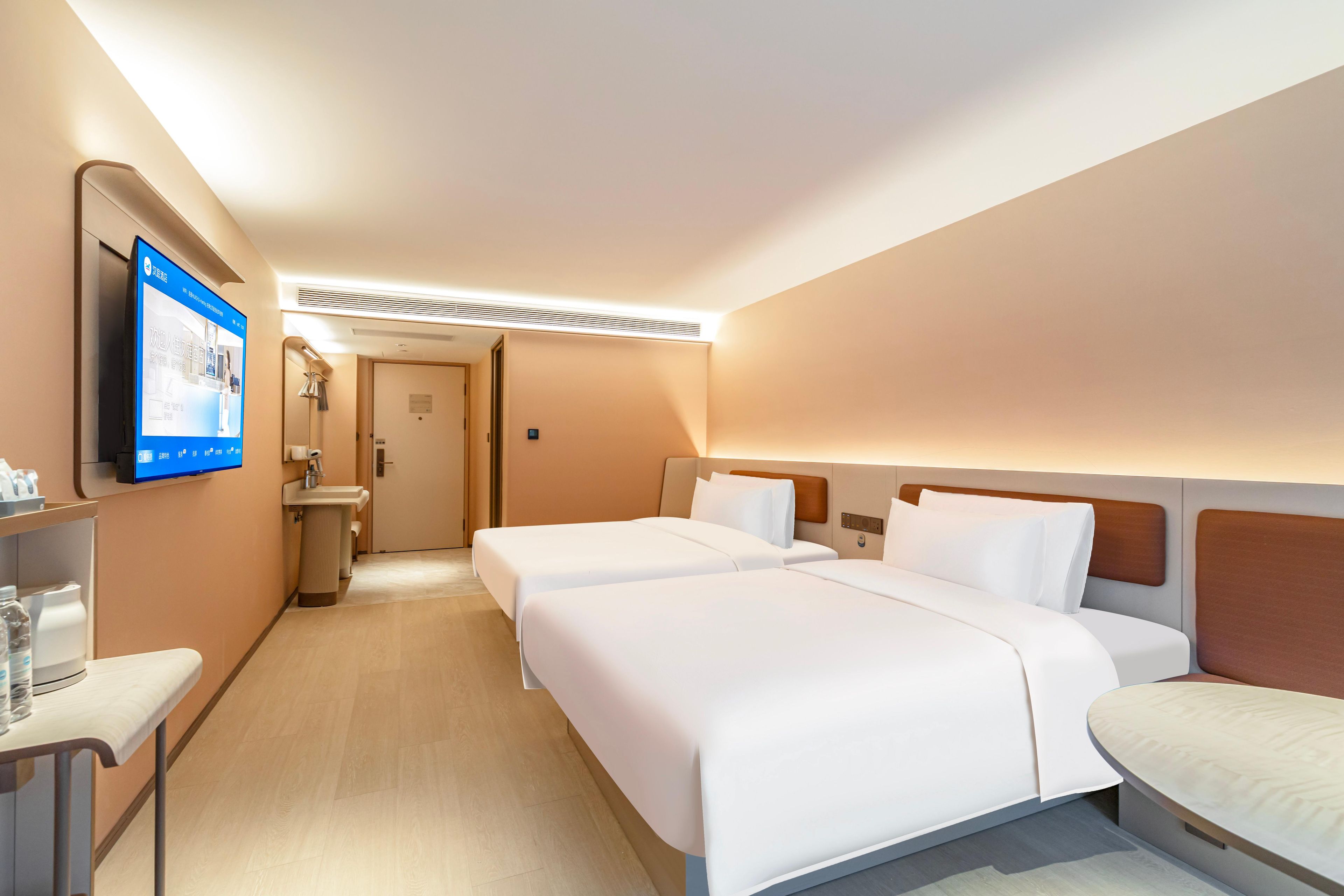 A hotel room with two beds, a TV, a desk, and a bathroom.
