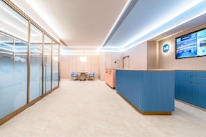 A modern reception area with a blue counter, a digital screen displaying information, and a seating area with a table and chairs. - Hanting Hotel (Xi'an)