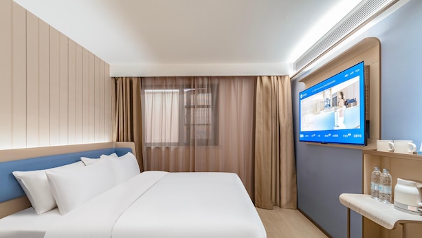 A hotel room with a bed, a TV mounted on the wall, a desk with a chair, and a window with curtains. - Hanting Hotel (Xi'an)