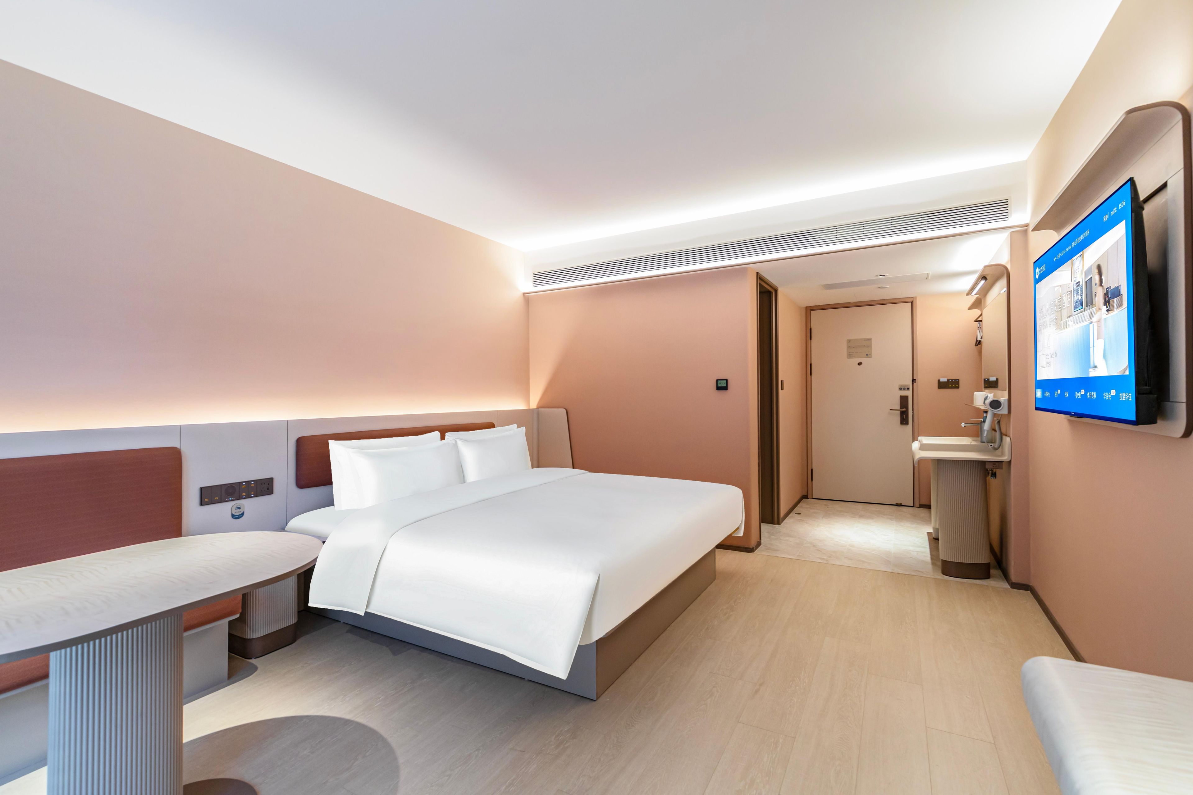 A hotel room with a bed, bedside table, and a TV mounted on the wall.