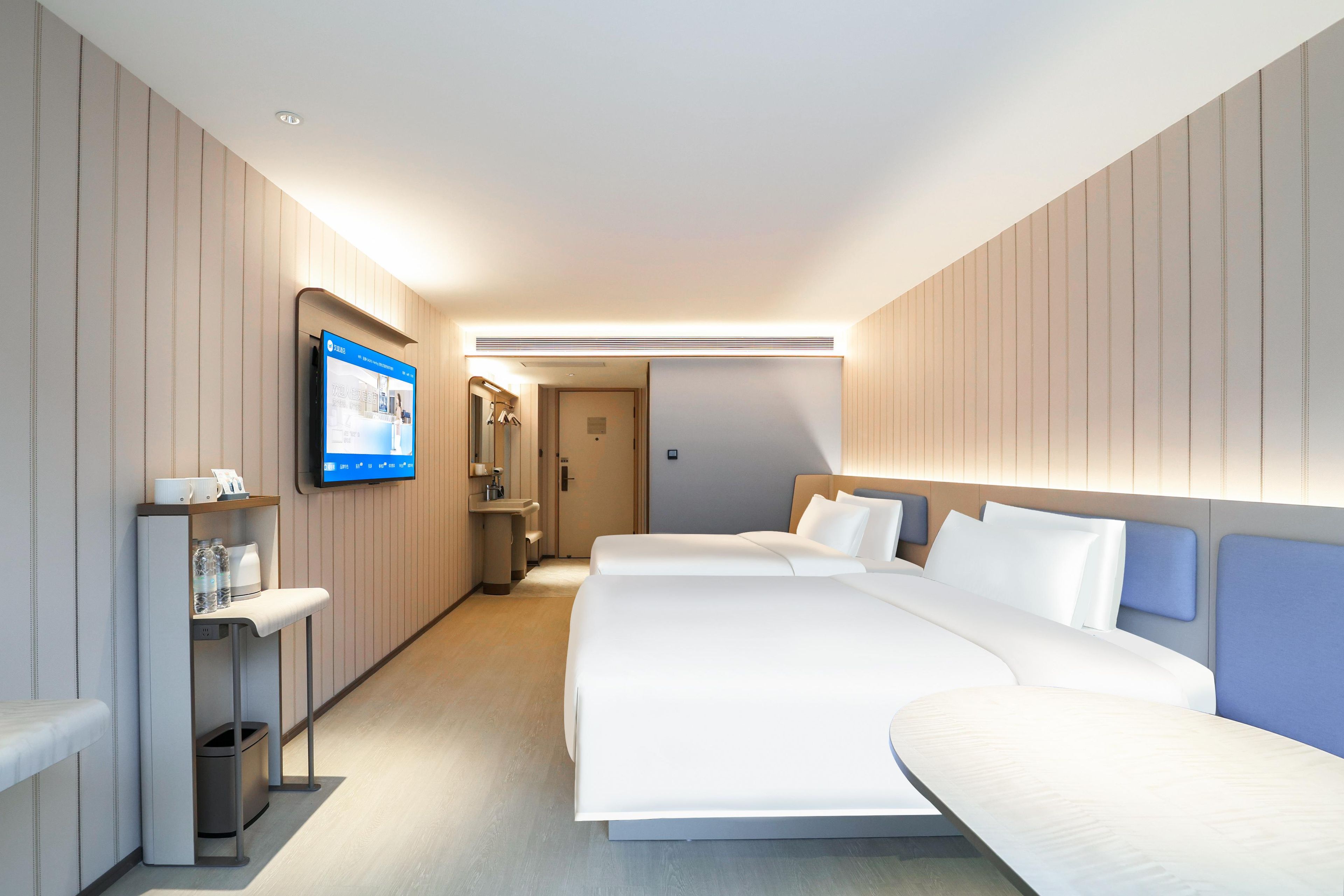 A hotel room with a large bed, a TV mounted on the wall, and a small desk with a trash bin.