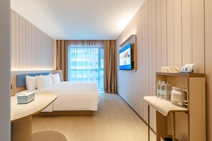 A hotel room with a bed, bedside table, and a desk with a chair. There is a television mounted on the wall and a window with curtains. - Hanting Hotel (Xi'an)