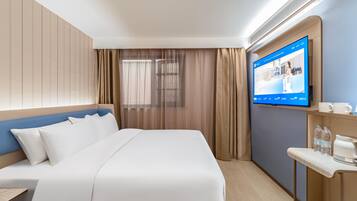 Habitación de hotel con cama, televisor montado en la pared, escritorio con silla y ventana con cortinas.
