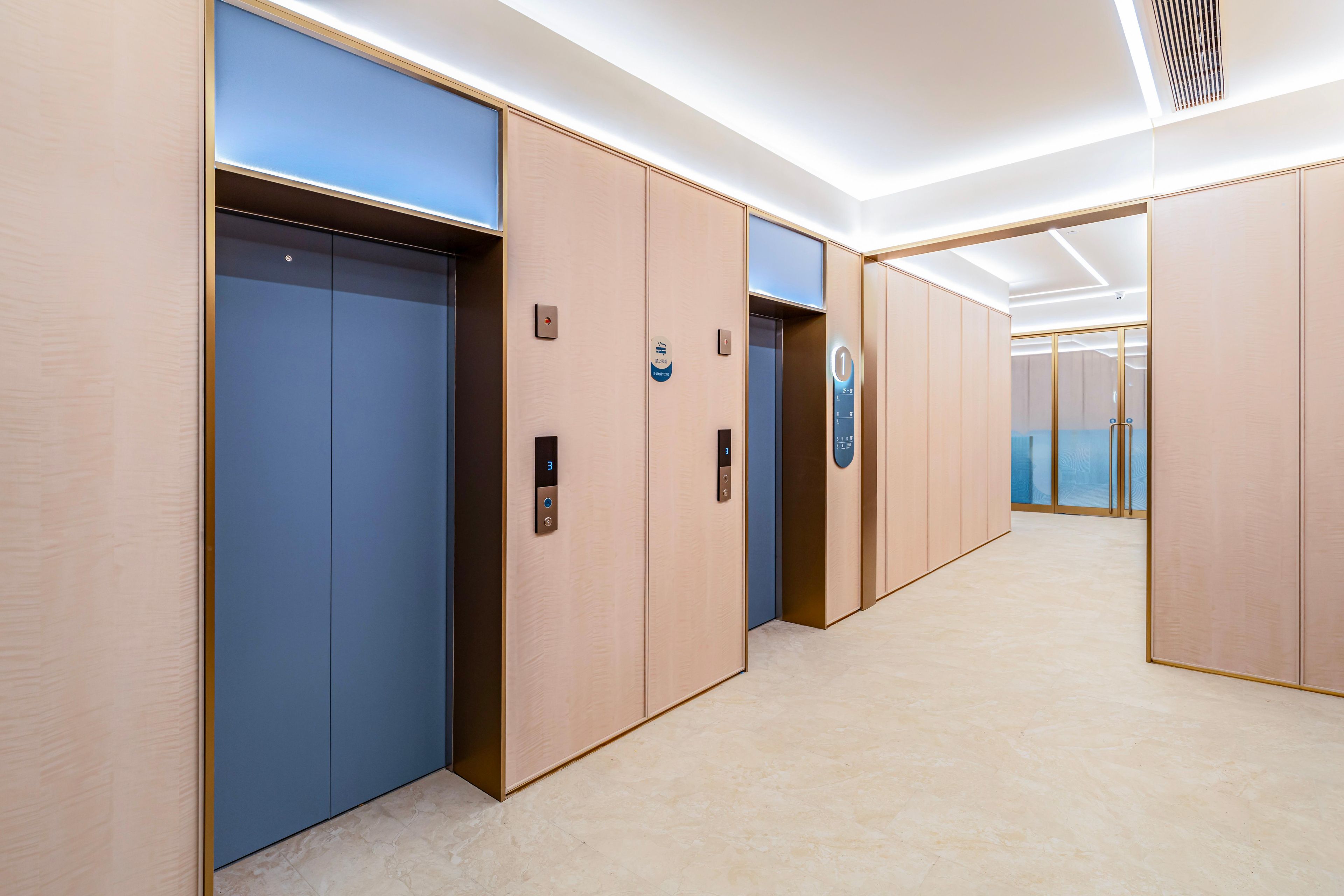 Un área de ascensores moderna con puertas de color azul y beige, indicadores digitales de pisos y un piso de baldosas impecable.
