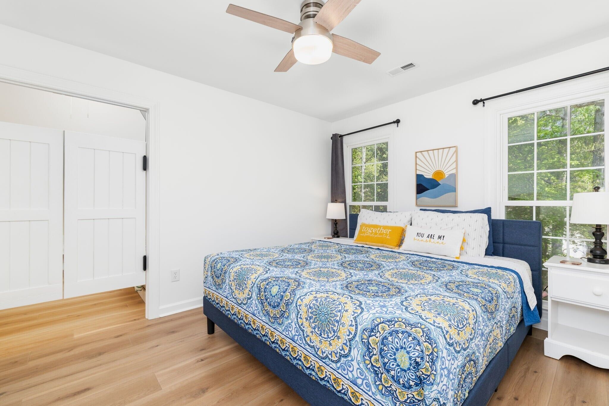 Un dormitorio con cama, ventilador de techo, ventana con cortinas y una puerta.