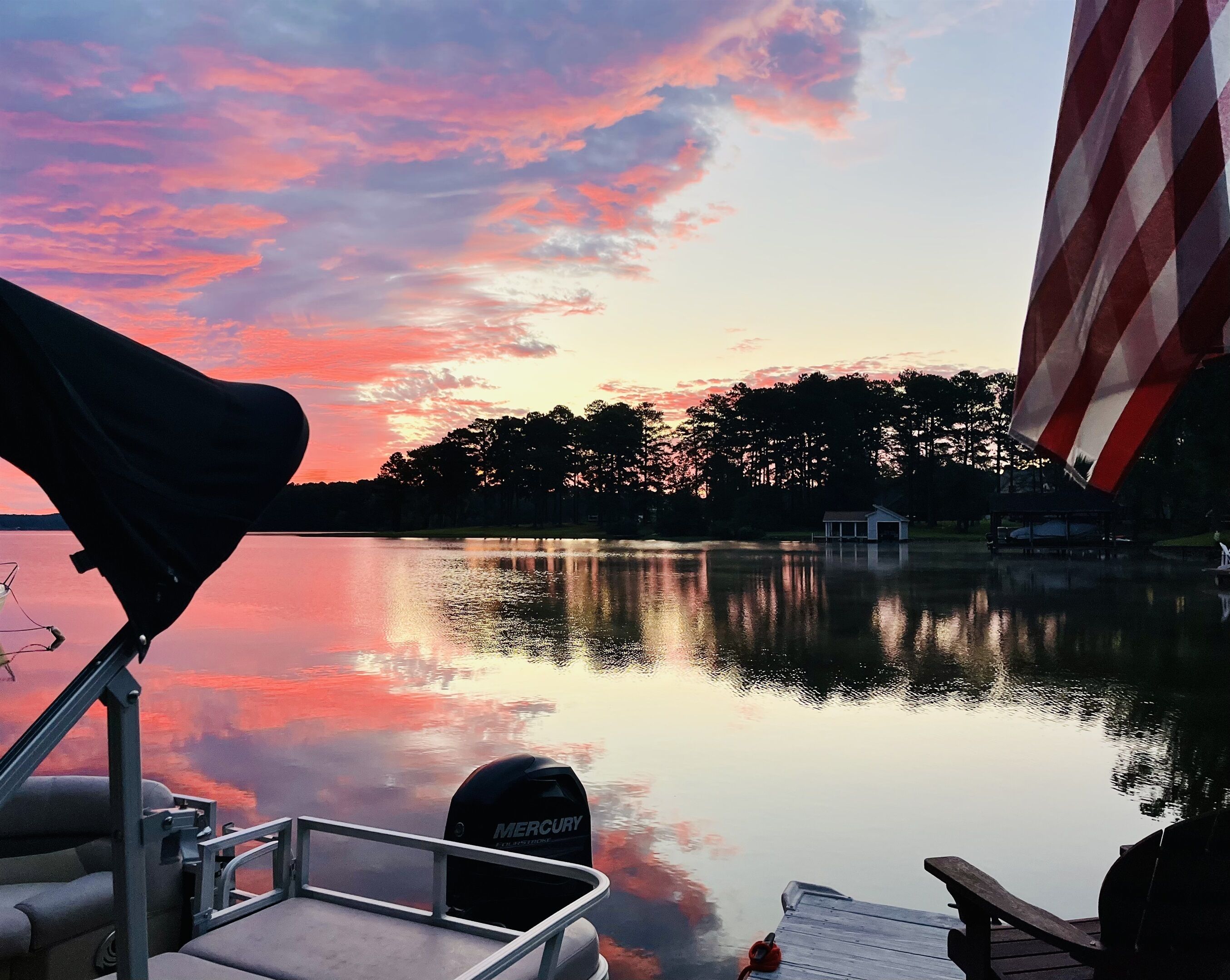 A boat docked at a calm lake with a sunset in the background.