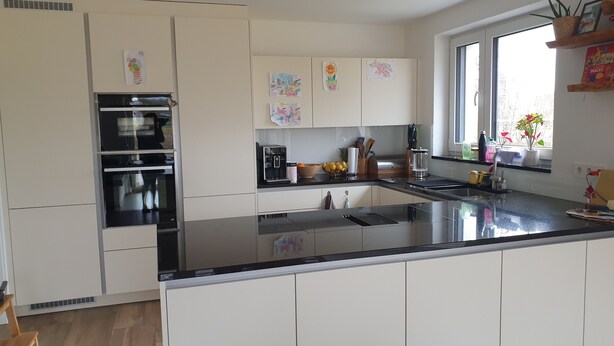 Una cocina moderna con armarios blancos, encimera negra y horno empotrado. Hay una ventana con vistas al exterior, y un estante con objetos decorativos.
