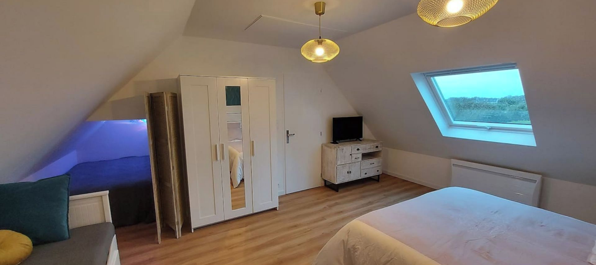 Ett sovrum med ett sluttande tak, en garderob, en tv-apparat på en byrå, en säng och ett takfönster.