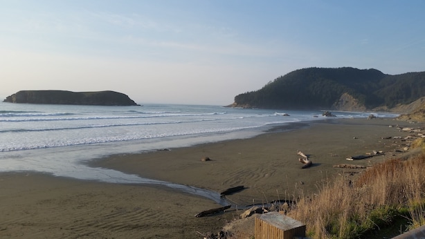 A beach with waves, a wooden structure, and a forested hill in the background. - Cornerstone Ranch experience minutes to the beach and Rogue River (Gold Beach)