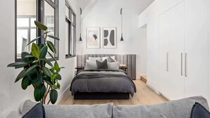 Een moderne slaapkamer met een bed, nachtkastjes, een potplant en kunst aan de muur.