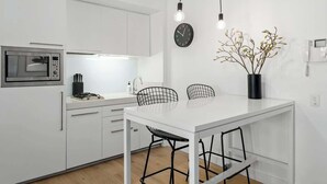 Een moderne keuken met witte kasten, een ingebouwde magnetron, een witte eettafel met zwarte stoelen van draadmetaal en hanglampen.