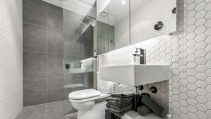 Een moderne badkamer met toilet, een douchecabine met glazen wanden en een witte wastafel met een betegelde achterwand van hexagontegels.