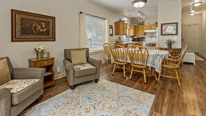 Un salon avec un canapé, des fauteuils, une table à manger avec des chaises, un tapis et, au fond, une cuisine.