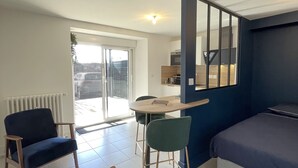 A modern, well-lit room with a bed, two chairs, a small table, and a kitchen area visible through a glass door. - Town Hall Studio - Hyper-center Limoges (Limoges)